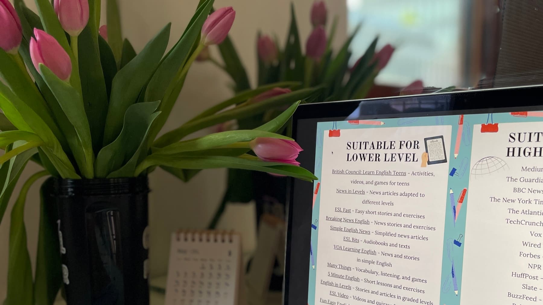 Laptop z listą anglojęzycznych materiałów podzieloną na poziomy, obok bukiet różowych tulipanów